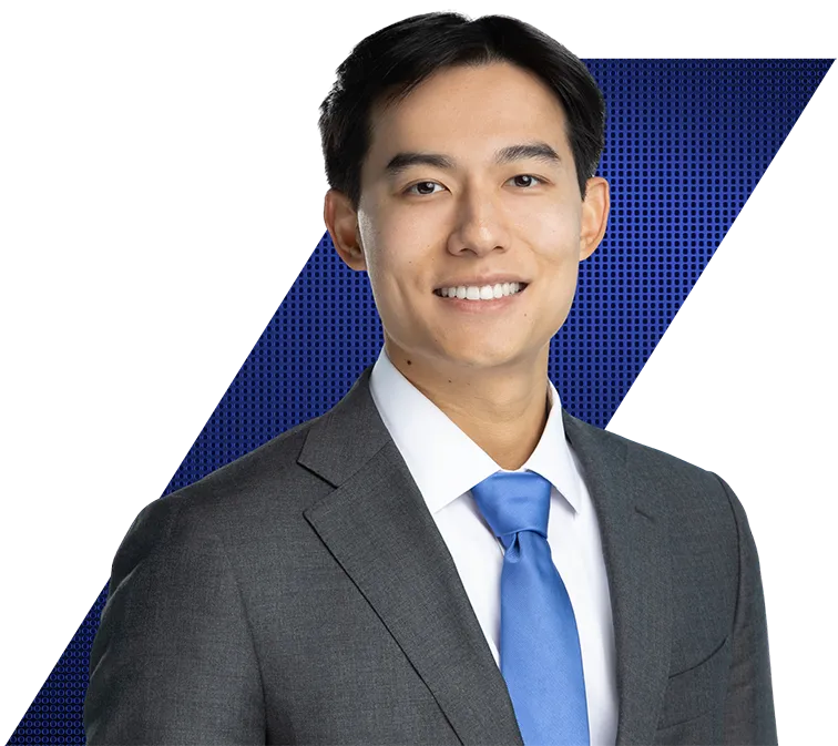 Headshot of a smiling East Asian man in a grey suit, white shirt, and blue tie against a black and blue patterned background.