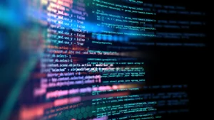 Close-up of glowing computer code in vibrant blue, purple, and red hues on a dark background, with some lines in focus and others blurred.