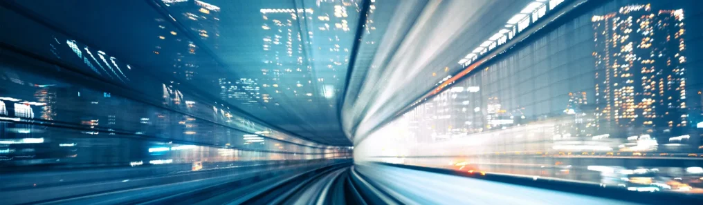 View from a fast-moving train at night, showing blurred city lights and tracks streaking forward, conveying high speed and urban energy.