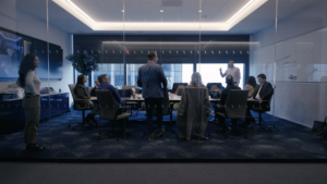 A group of Vista Equity Partners and Asset employees in a modern glass-walled conference room with a large table and screens.