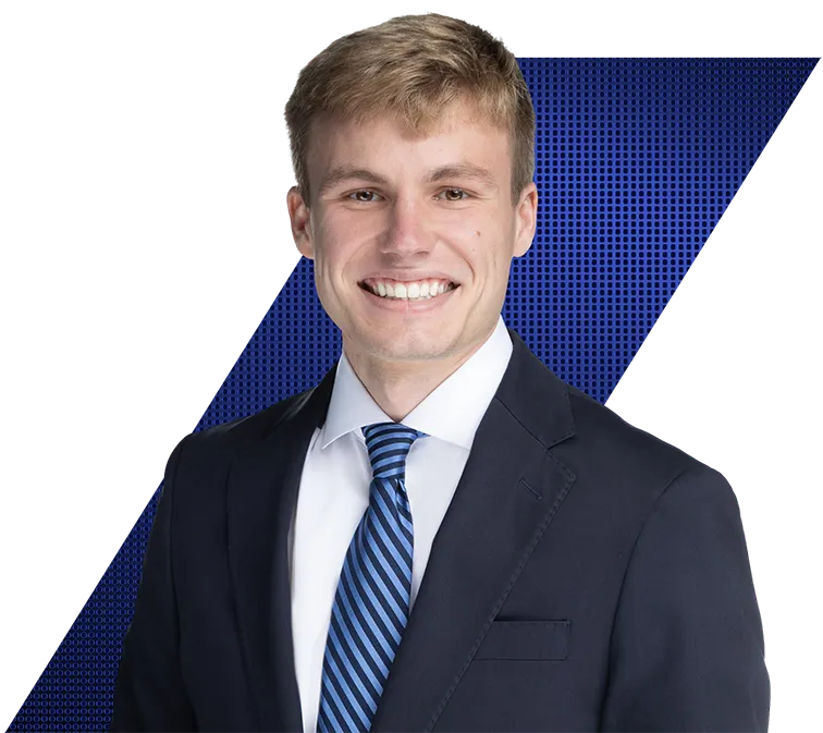 Headshot of a smiling young man with light brown hair, wearing a dark blue suit, white shirt, and striped blue tie against a black and blue geometric background.