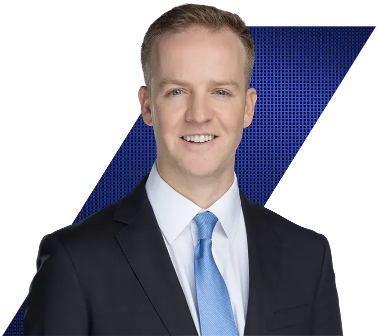 Headshot of a smiling man with light hair and blue eyes, wearing a dark suit and light blue tie, against a black and blue geometric background.